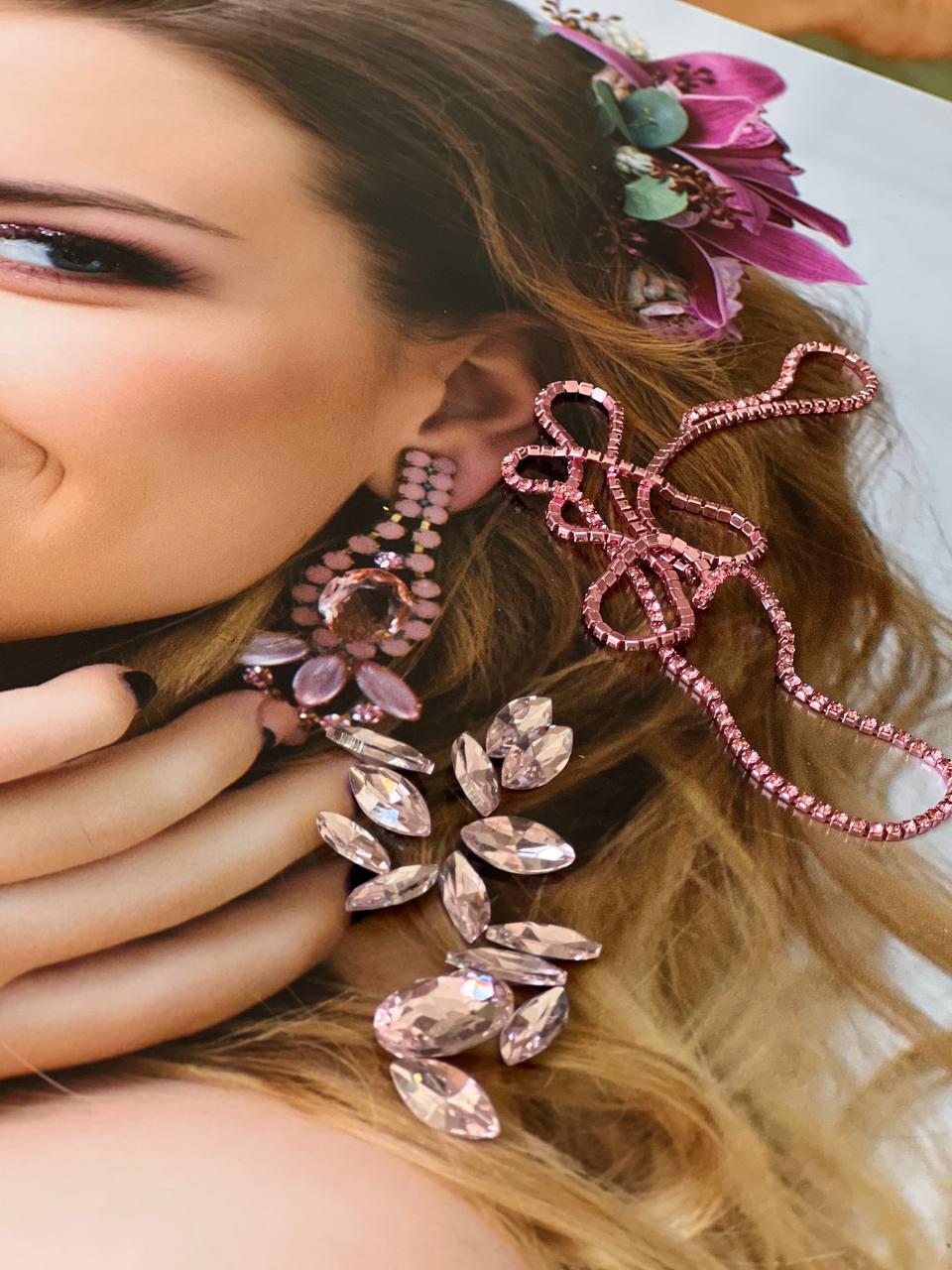 Close-up of a rhinestone drop earring and jeweled hairpiece styled against soft floral tones